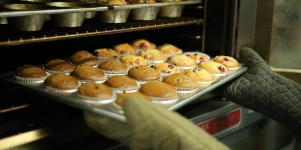 baker pulls a tray of fresh muffins from a commercial oven, representing the food service small businesses CADDA supports with affordable loans.